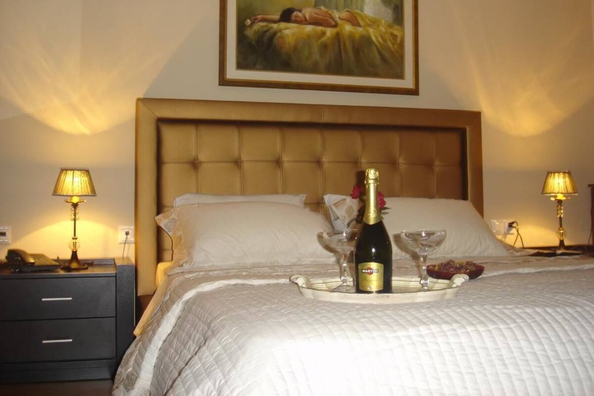 Een hotelkamer met een groot bed, een nachtkastje, een bedlampje, een dienblad met champagne en een schilderij aan de muur.