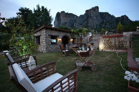 A stone building with a small porch, outdoor seating, and a view of rocky mountains.