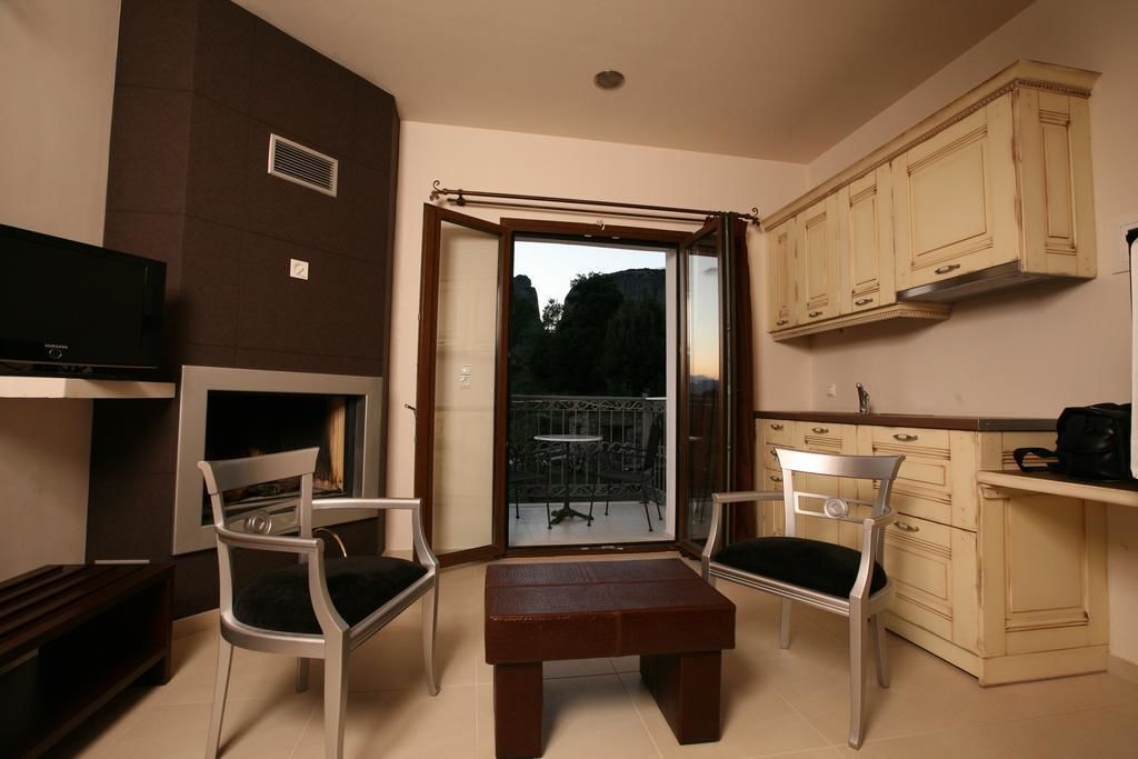 Una habitación pequeña y acogedora con chimenea, dos sillones, una mesa y una zona de cocina con armarios y televisor.