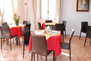 A dining area with a table set for four, chairs, a vase of flowers, and a painting on the wall.