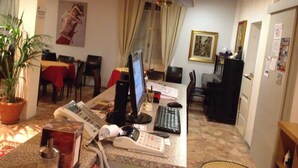 A hotel lobby with a reception desk, a computer, a telephone, and a dining area with tables and chairs. - Hotel Domodossola (Domodossola)