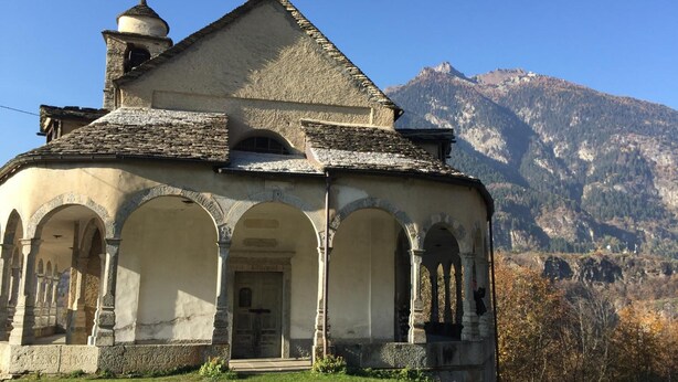 A historic church with a bell tower, arched entrance, and a mountainous backdrop. - Hotel Domodossola (Domodossola)