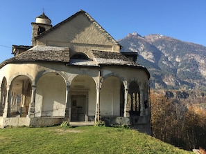 A historic church with a bell tower, arched entrance, and a mountainous backdrop.