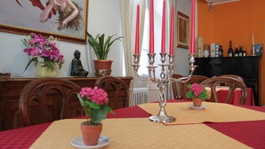 A dining area with a table set for two, surrounded by wooden chairs. A candelabra with red candles is placed on the table. There are potted plants on the table and a statue on the wall. - Hotel Domodossola (Domodossola)