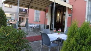 An outdoor patio with a covered seating area, a table with a white tablecloth, and a potted plant. - Hotel Domodossola (Domodossola)
