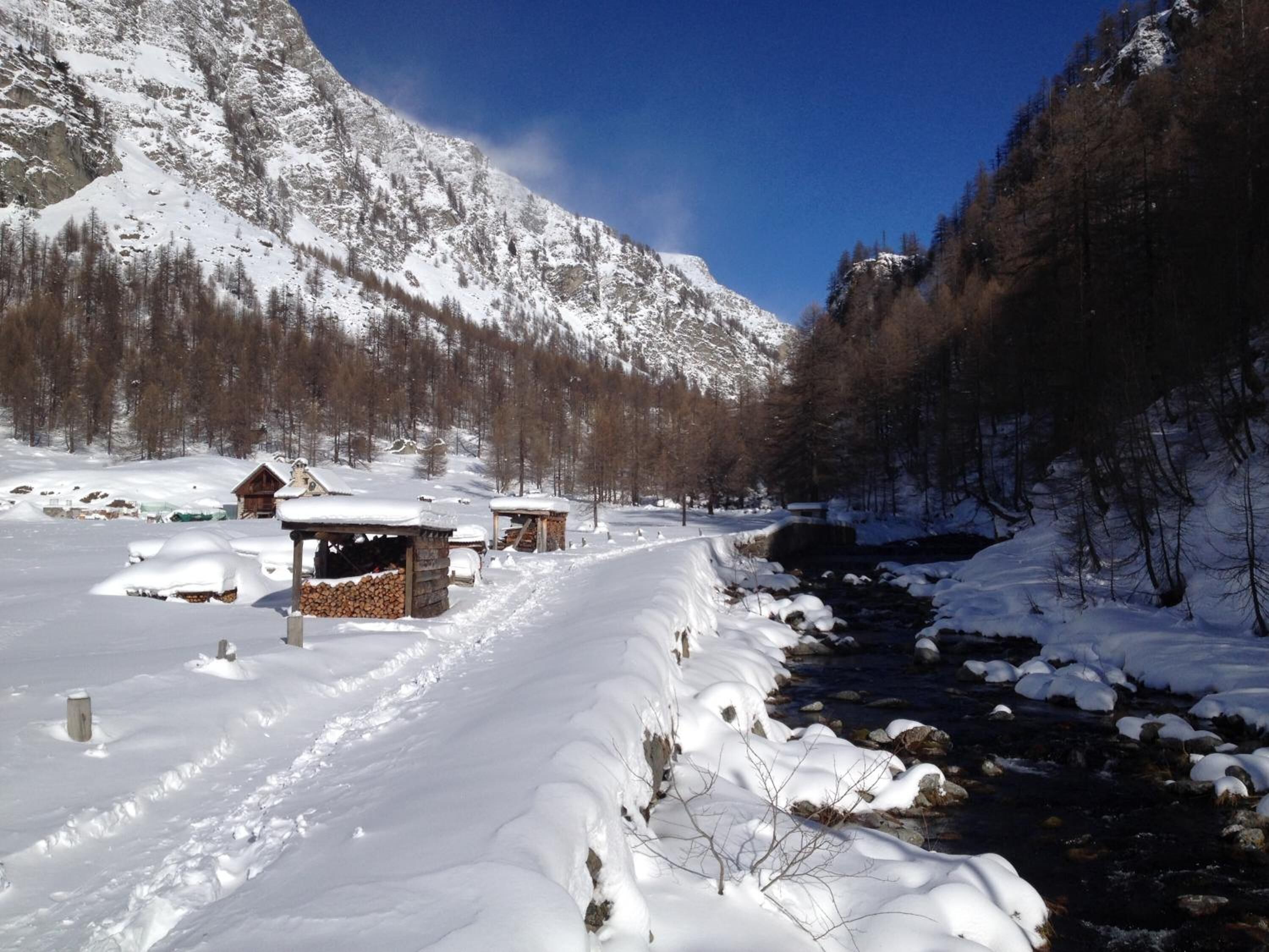 Eine verschneite Berglandschaft mit Holzhütten und einem Bach.