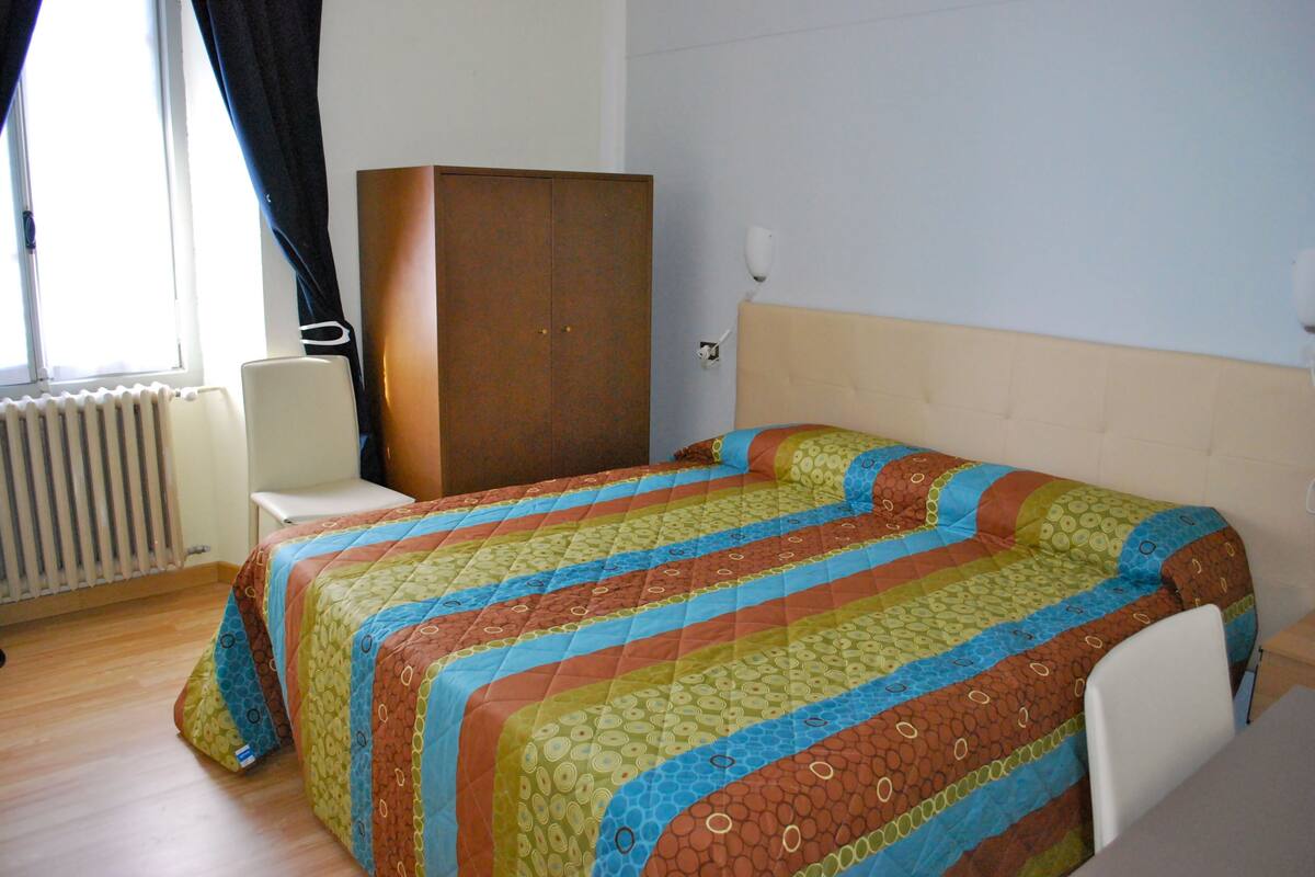 Une chambre à coucher avec un lit, un radiateur, une armoire et une fenêtre avec des rideaux.
