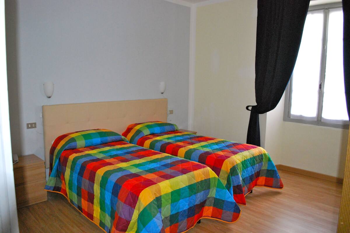Une chambre avec deux lits, un plancher en bois et une fenêtre avec un rideau noir.