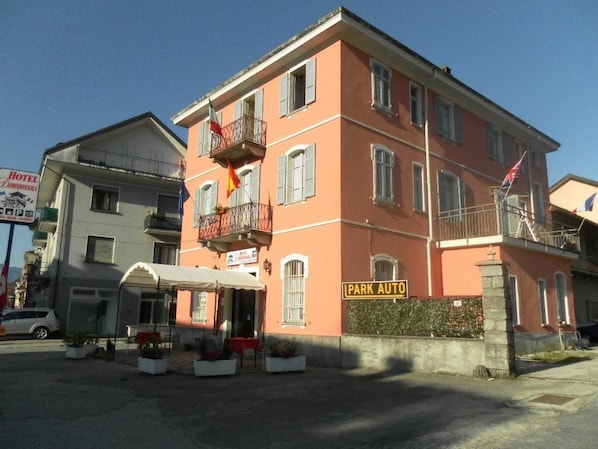 A multi-story hotel with a balcony, a sign for 'PARK AUTO', and a visible entrance with a canopy.