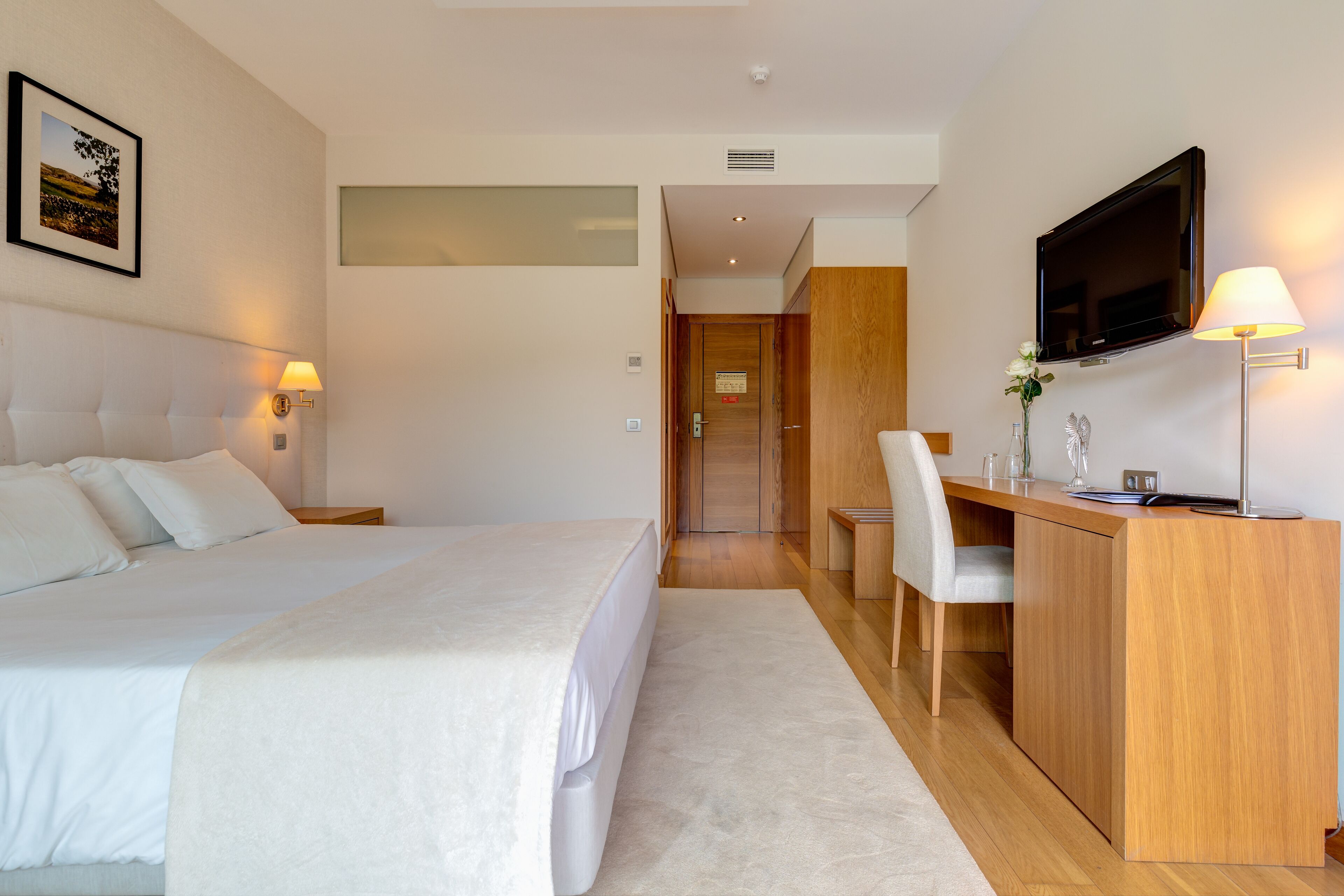 A hotel room with a bed, desk, chair, TV, and a framed picture on the wall.