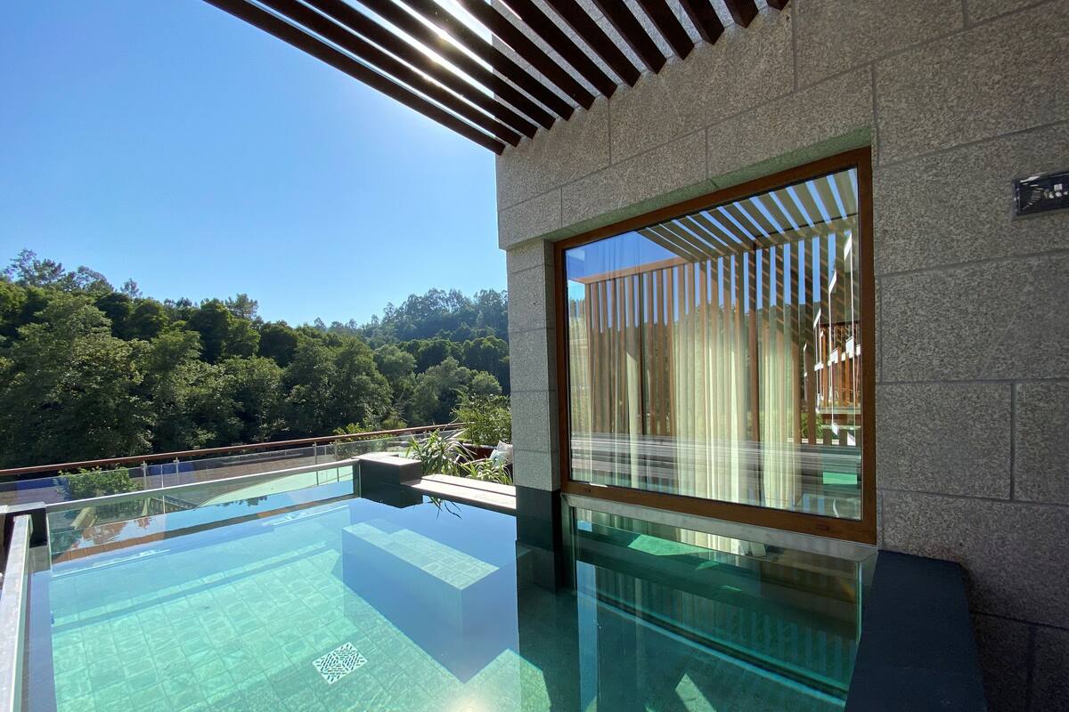 A modern infinity pool with clear water, surrounded by stone walls and a wooden pergola.