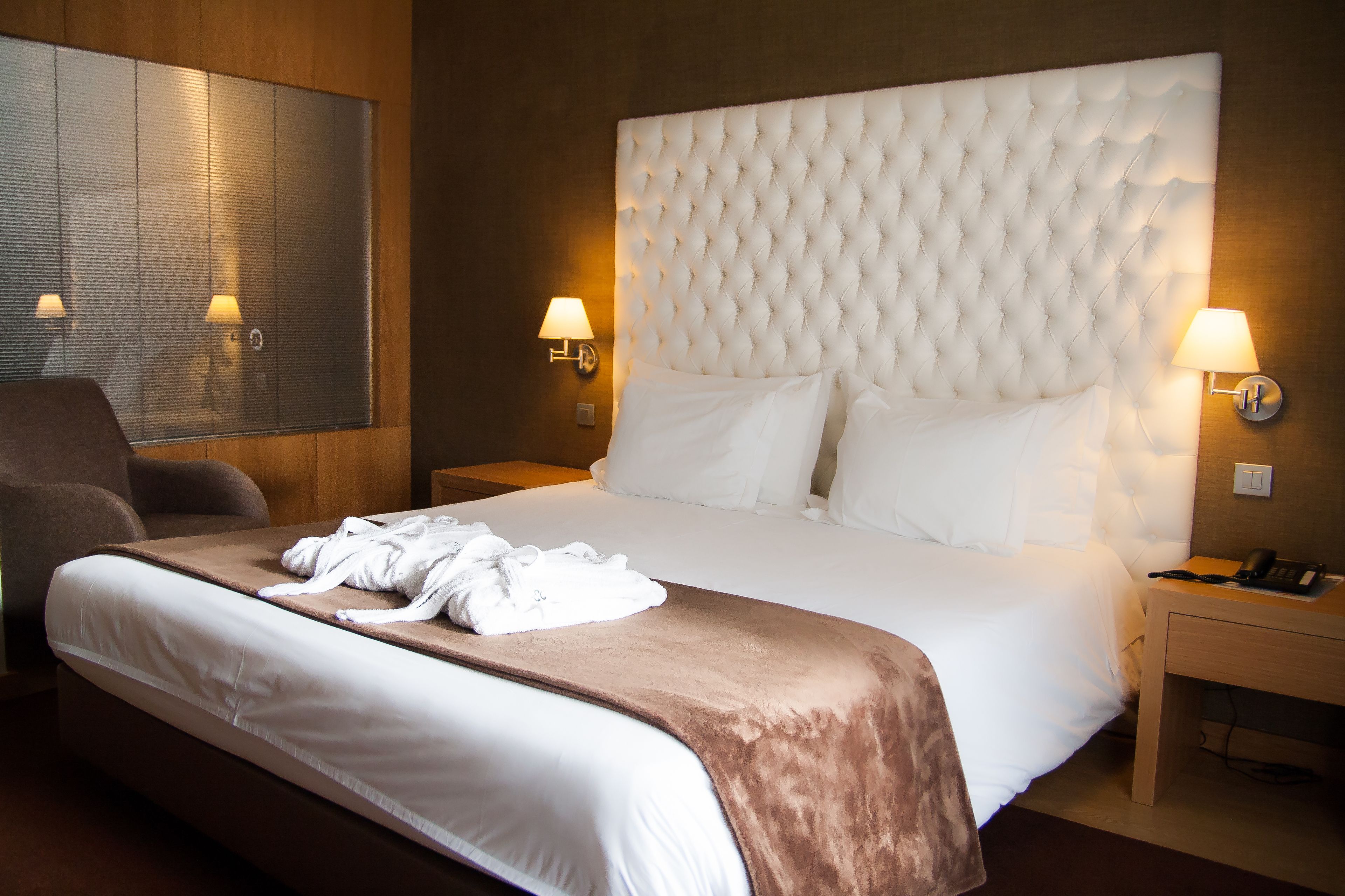 Habitación de hotel con una cama grande, dos lámparas de noche, un cabecero de madera y un espejo grande en la pared.