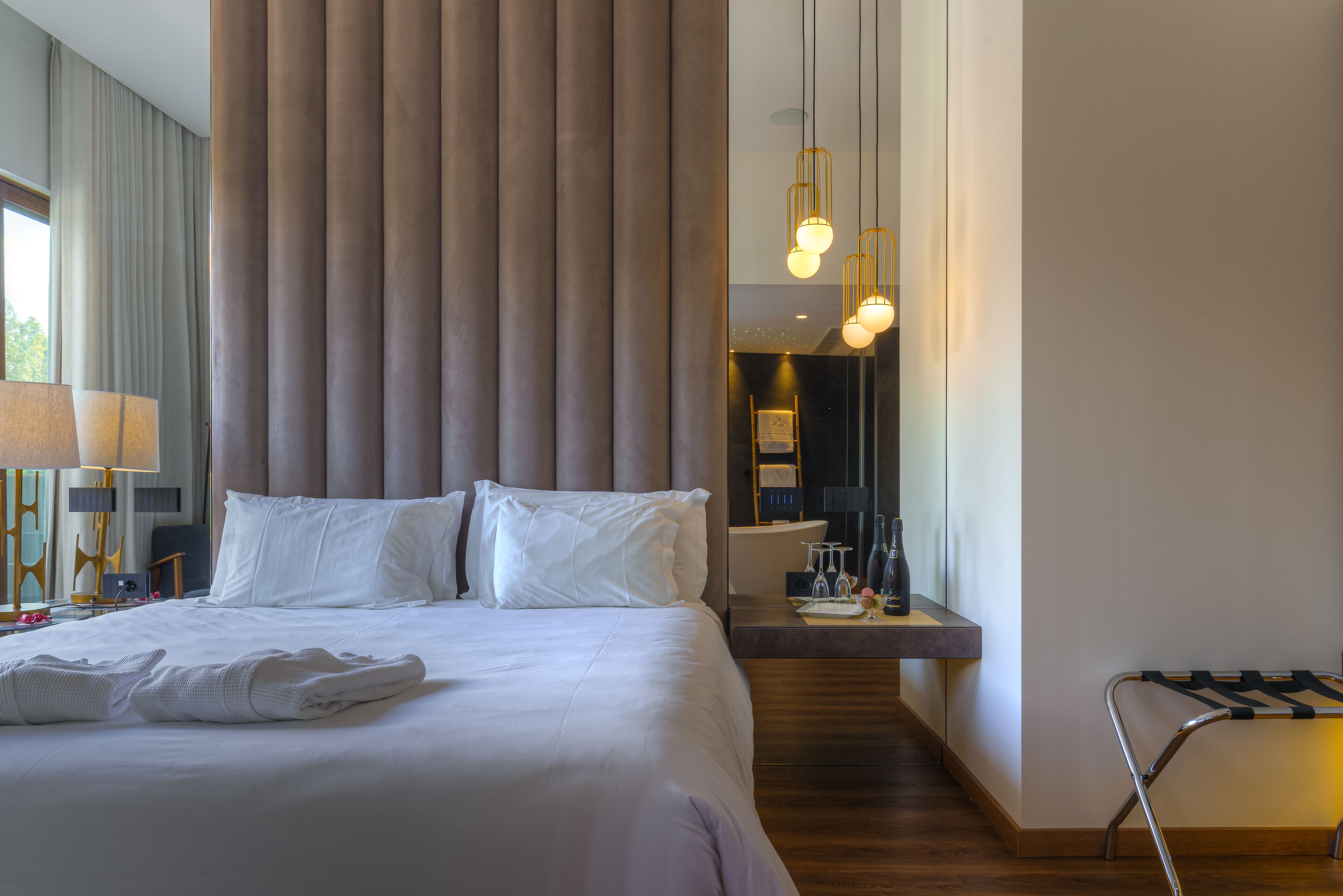 Ein Hotelzimmer mit einem großen Bett, einem Nachttisch mit Lampe, einem Spiegel und Blick auf den Flur.