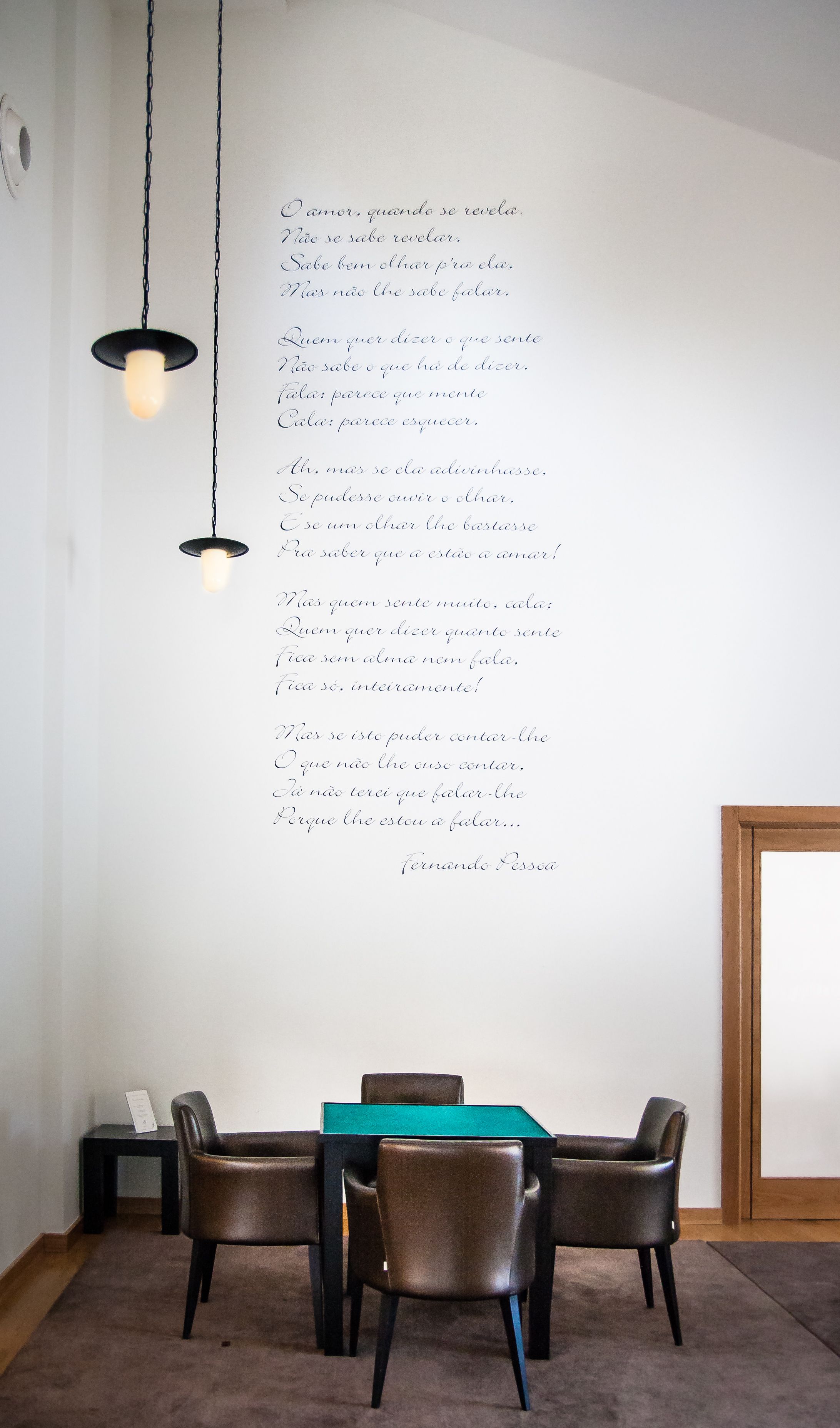 Uma sala de jantar com mesa e cadeiras, um lustre pendurado e uma parede com um poema.