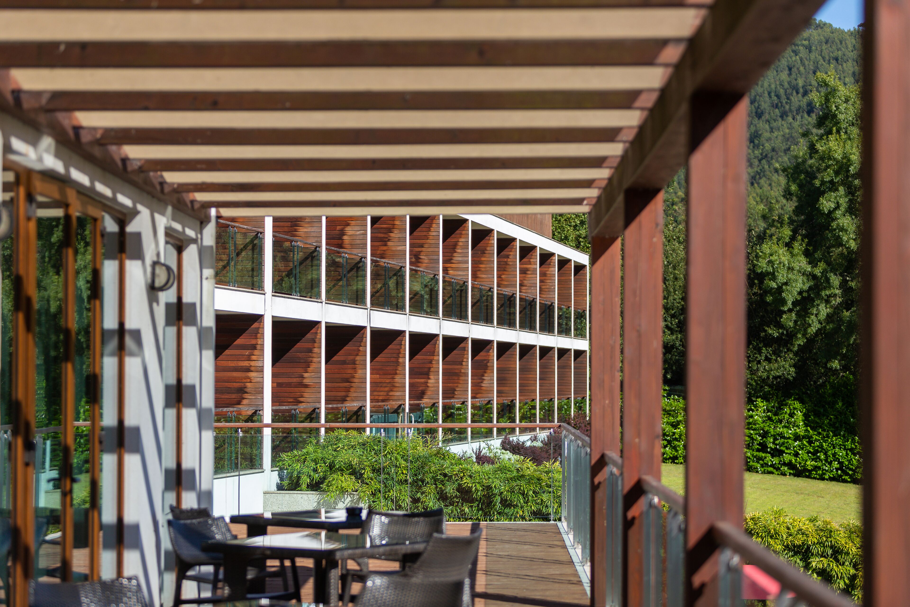 A covered outdoor seating area with a view of a modern building and lush greenery.