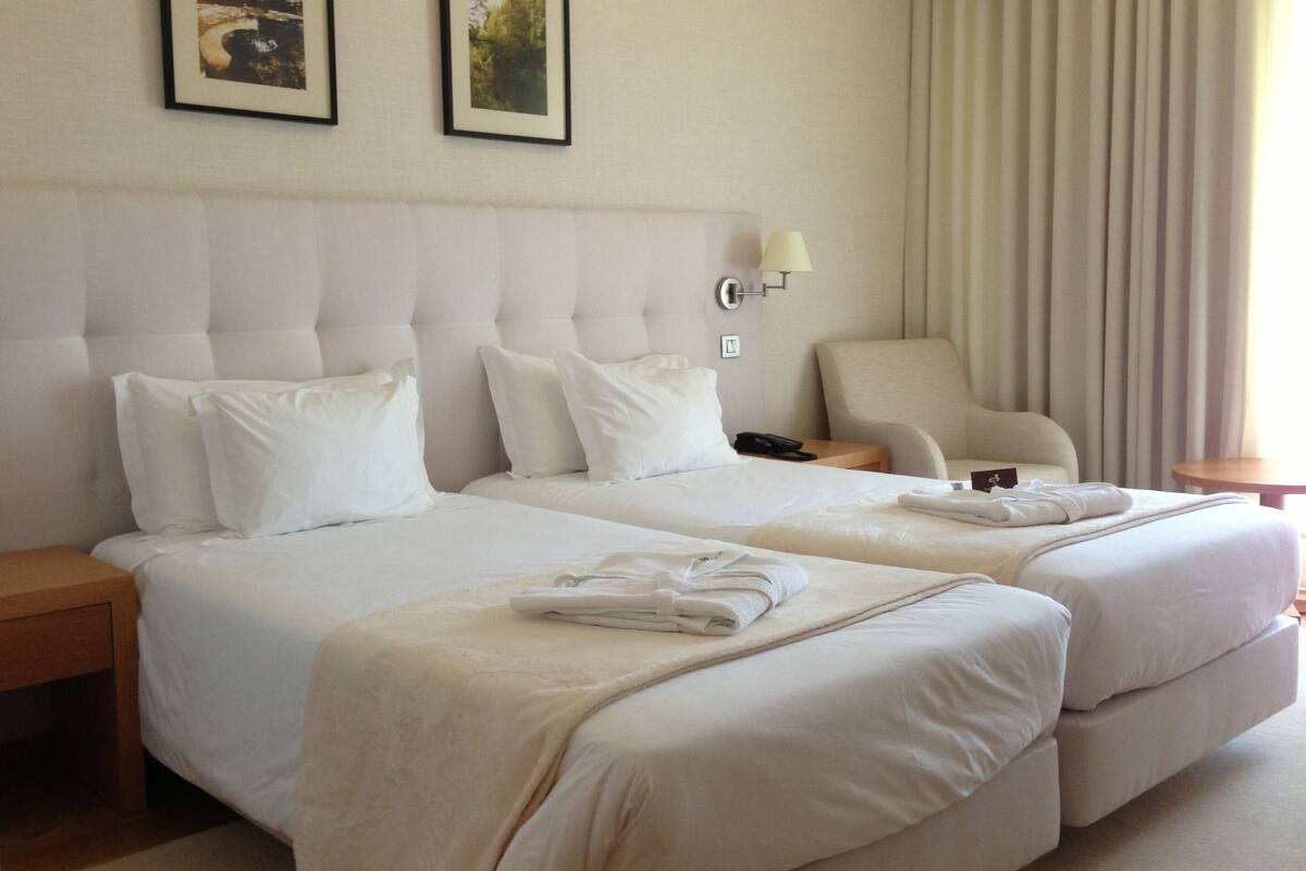 A hotel room with two beds, a chair, a nightstand, and a lamp.