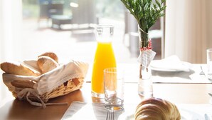 A breakfast setting with croissants, orange juice, and a small plant on a table by a window.