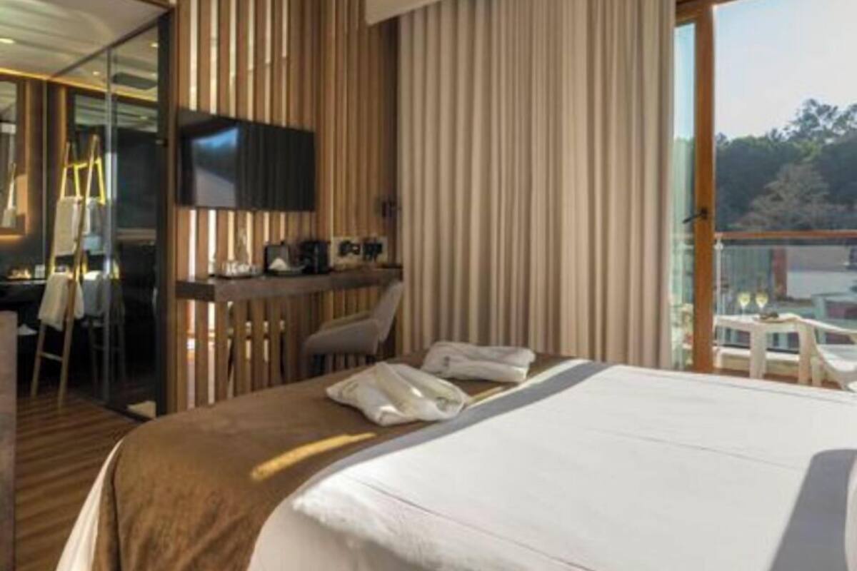 A hotel room with a bed, a desk, and a chair. There is a window with a view of trees and a building.