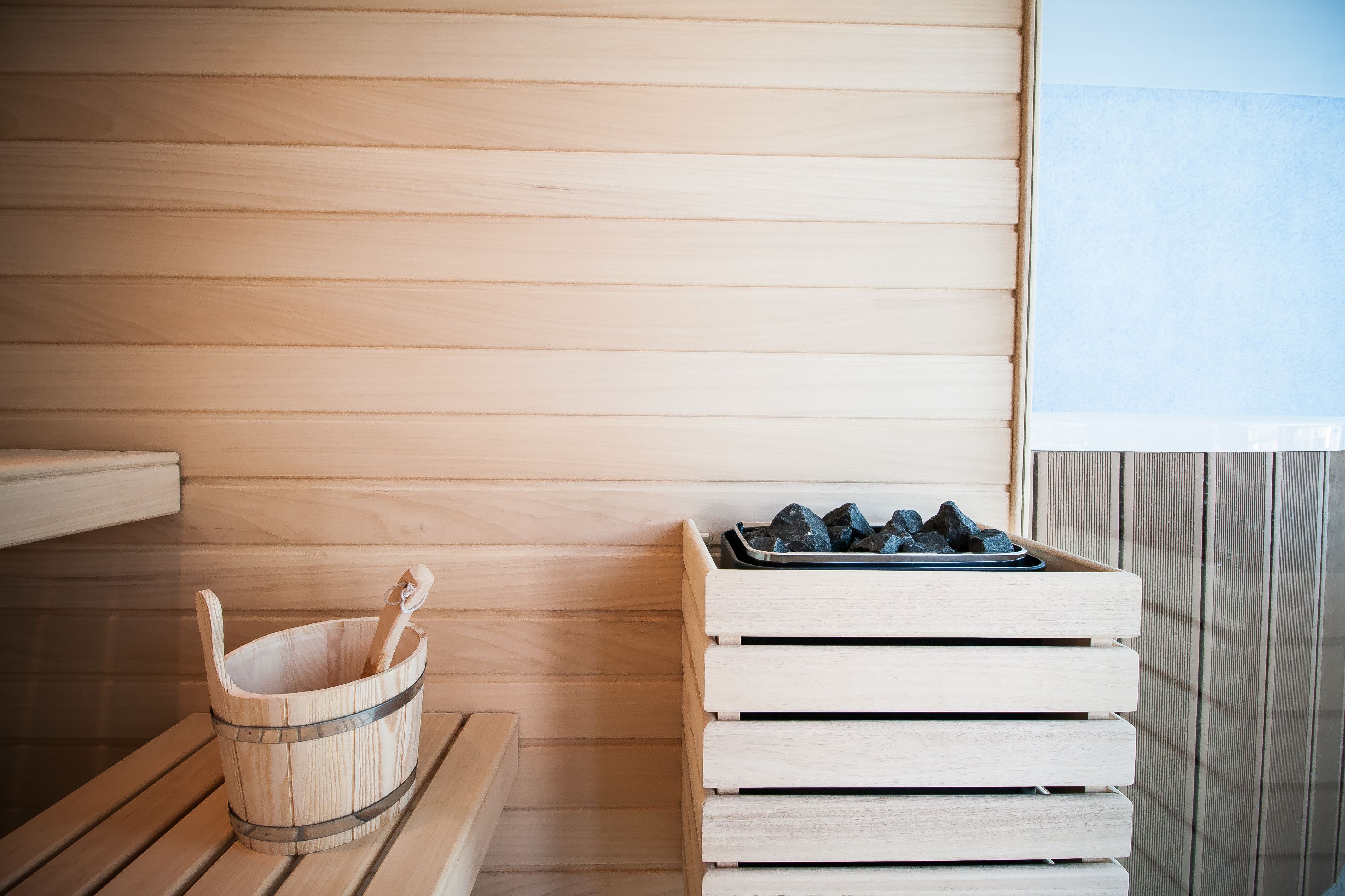 Un banco de sauna de madera, un cubo de madera con un palo de madera, y una pila de bancos de madera.
