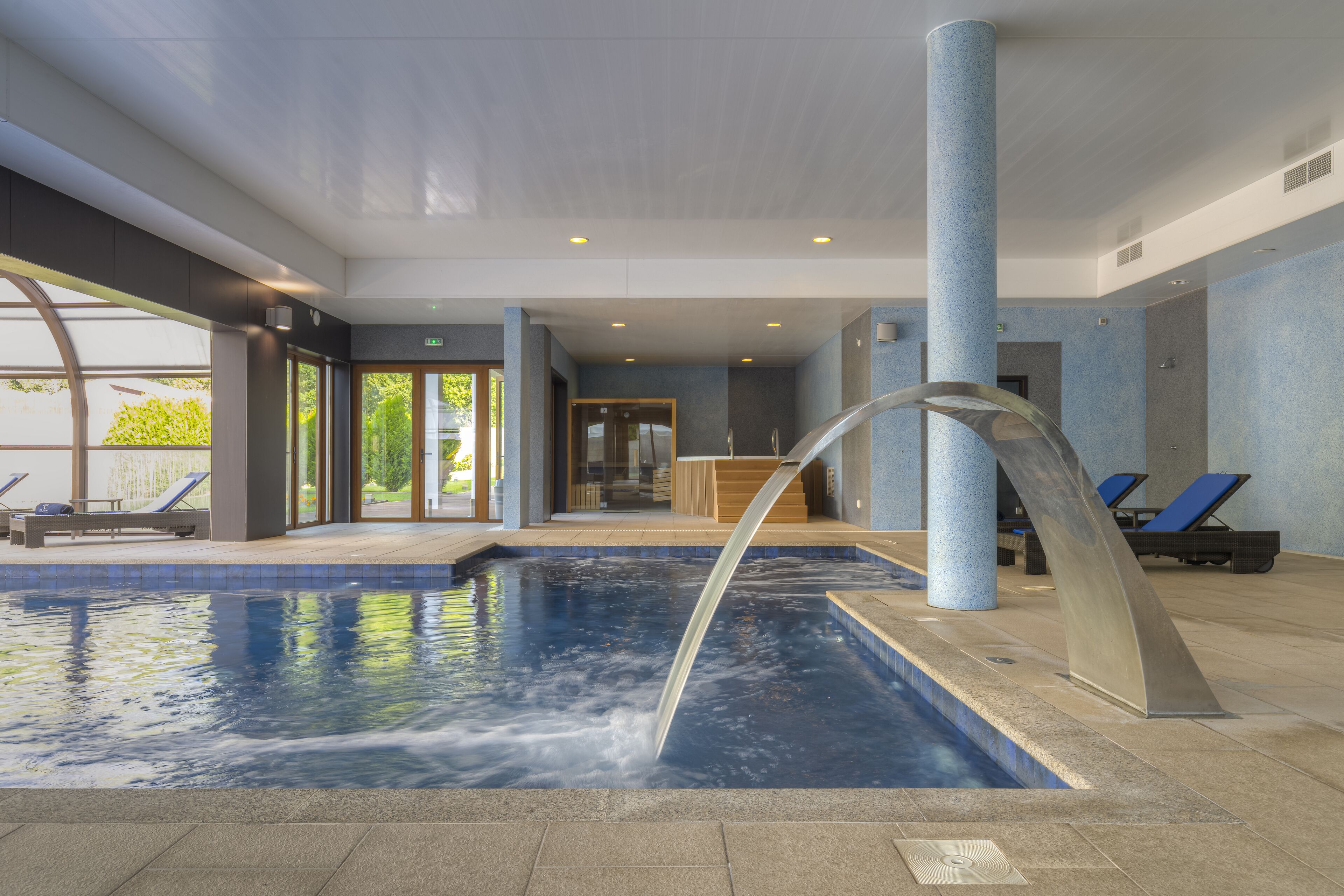 Una piscina interna con elementi d'acqua, sedie a sdraio e vista sull'esterno.