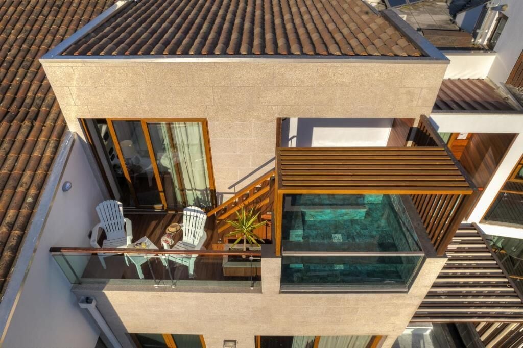 Un bâtiment moderne à deux étages, doté d’un balcon en verre, d’un petit espace extérieur aménagé en coin salon et offrant une vue sur les bâtiments environnants.