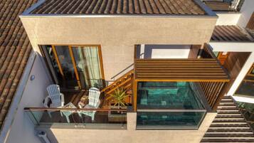 A modern two-story building with a glass balcony, a small outdoor seating area, and a view of the surrounding buildings.