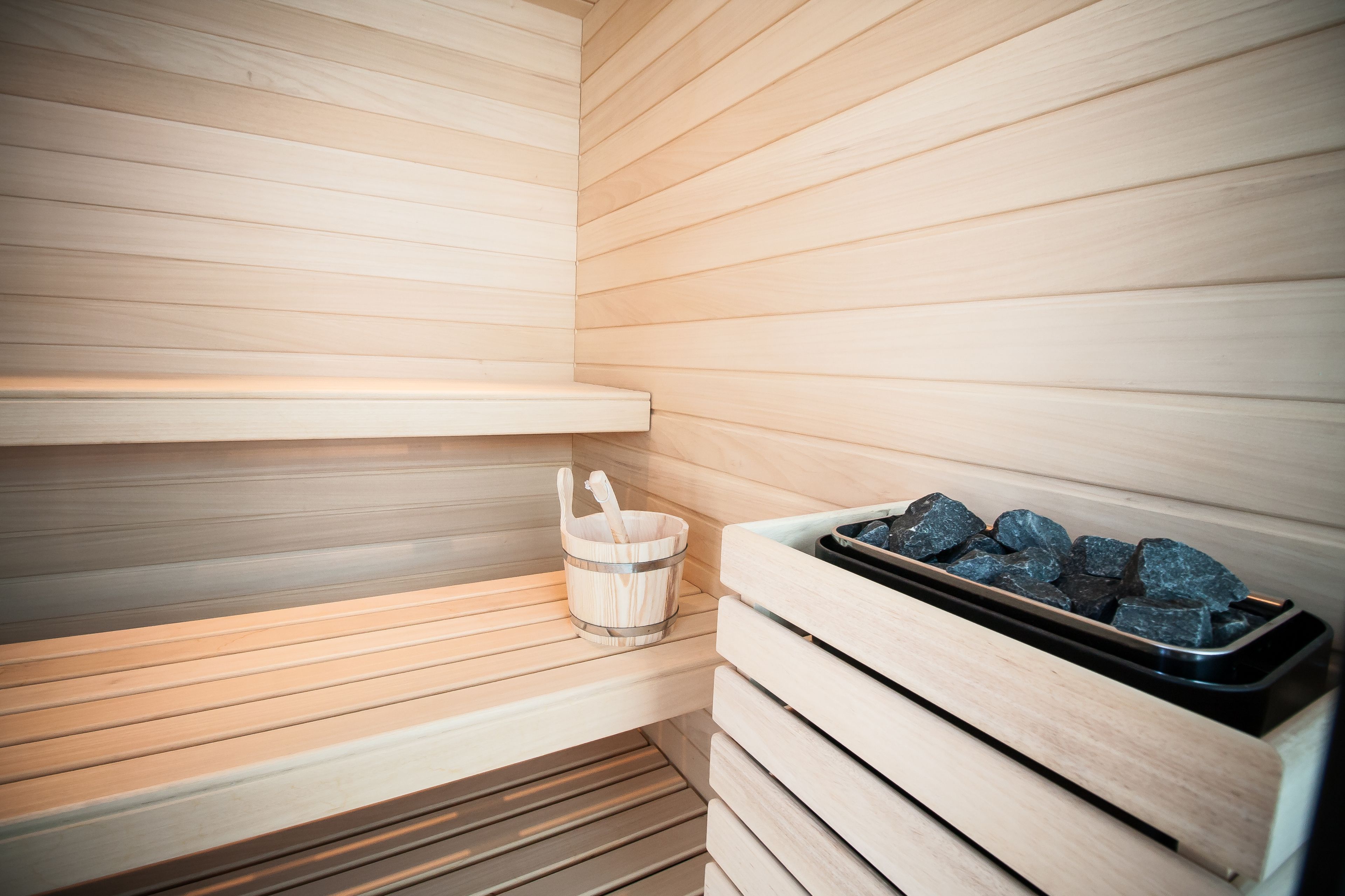 Una sauna amb seients de fusta, un cubell amb una escombra i una safata de pedres.