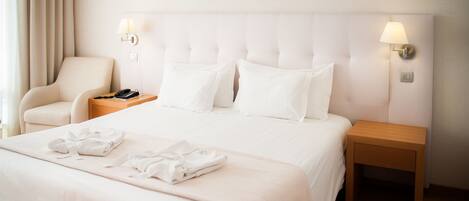 Una habitación de hotel con cama, una silla, una mesita de noche con lámpara y dos cuadros en la pared.