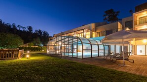 A modern house with a glass-enclosed swimming pool, outdoor seating, and a well-lit patio area.