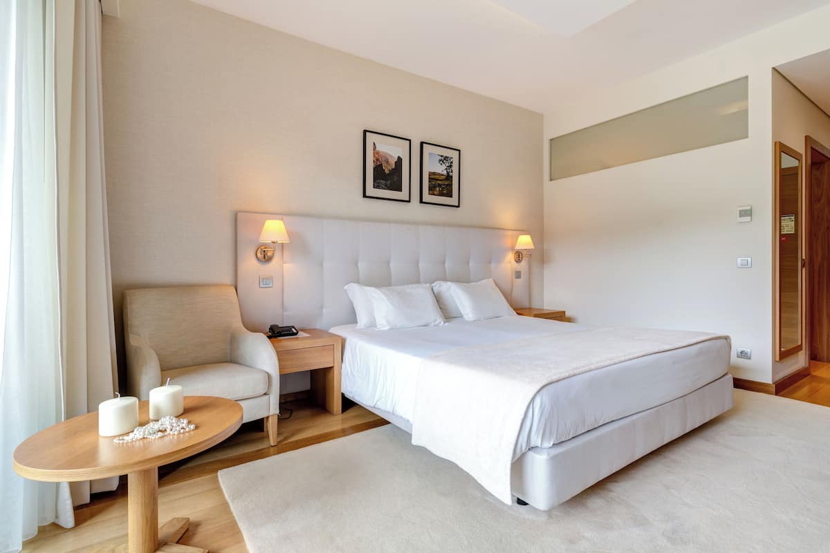 A modern hotel room with a large bed, a sofa, a round table with candles, and two wall-mounted lamps.