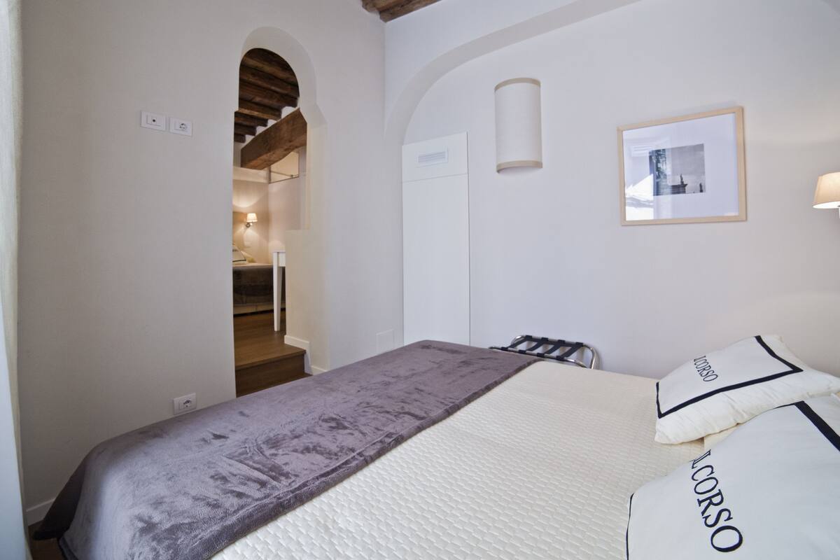 Un dormitorio con cama, un cuadro en la pared y una escalera que lleva a otra habitación.