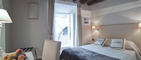 A hotel room with a bed, a desk with a fruit bowl, a chair, a window with curtains, and a wooden ceiling.