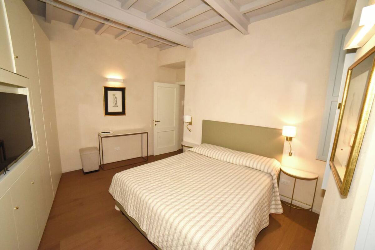 Un dormitorio con cama, mesita de noche, lámpara y un cuadro en la pared.