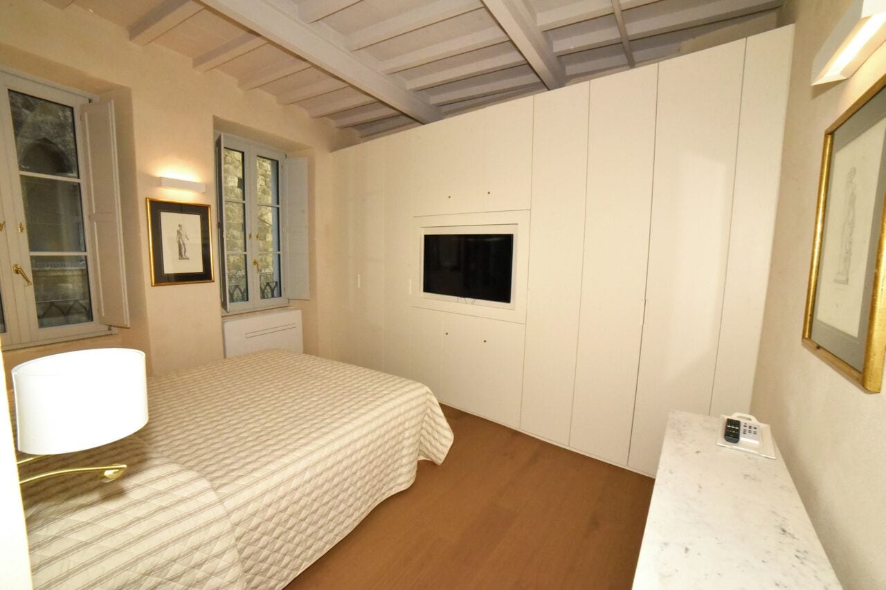 A bedroom with a bed, a bedside table, a lamp, a TV, and a framed picture on the wall.