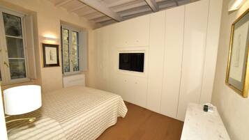 Un dormitorio con cama, mesita de noche, lámpara, televisión y un cuadro en la pared.