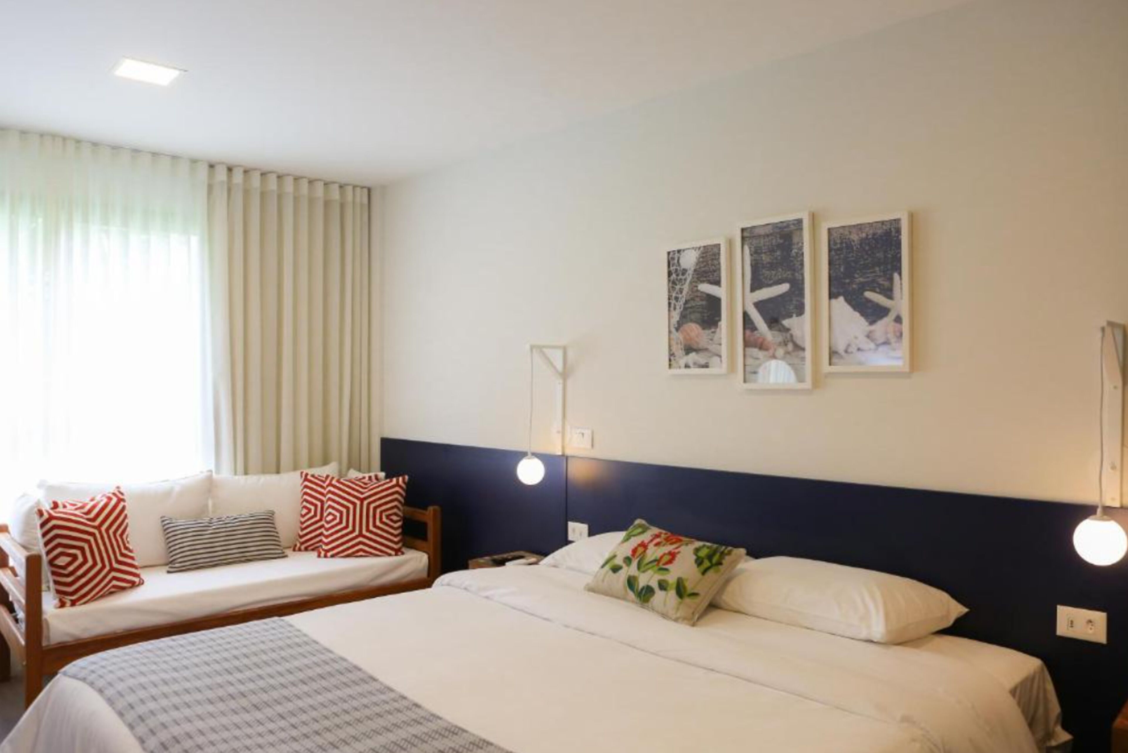A hotel room with two beds, a sofa, and a large window with curtains.