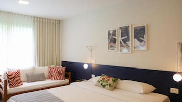 A hotel room with two beds, a sofa, and a large window with curtains.