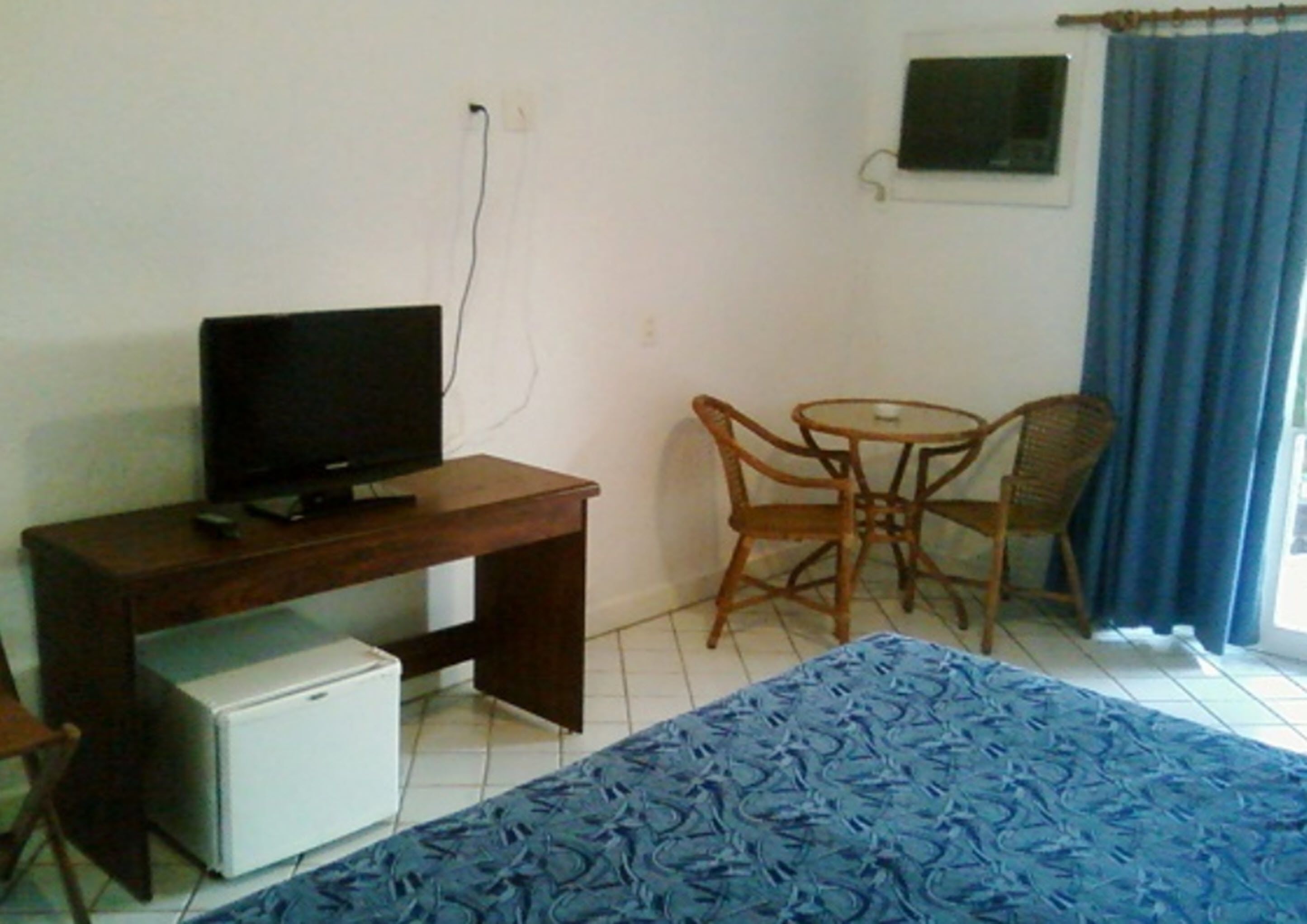 Una habitación pequeña con escritorio, televisión, refrigerador pequeño, una silla y un tapete estampado.