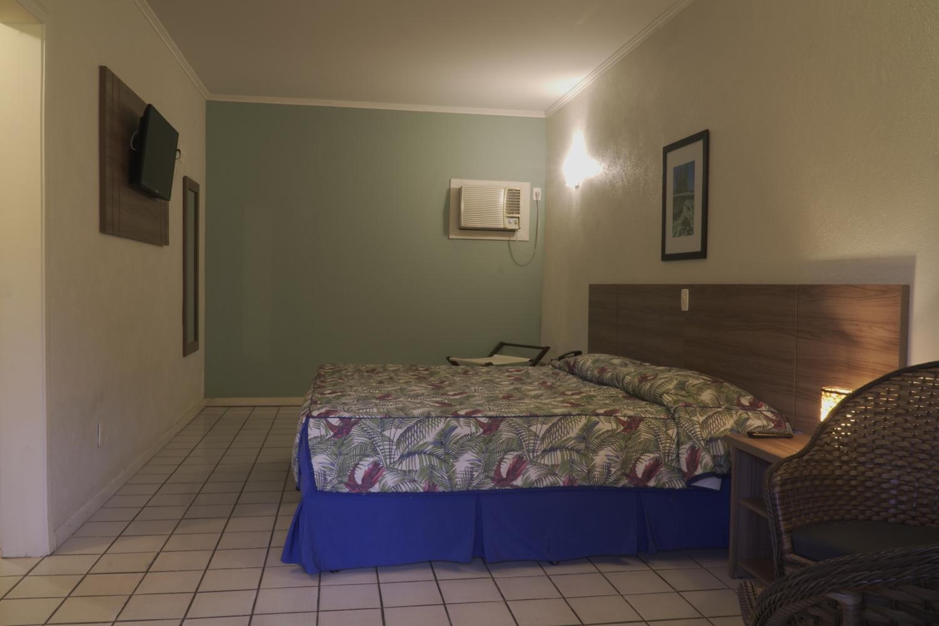 Un dormitorio con cama, una silla, aire acondicionado de pared y un cuadro en la pared.