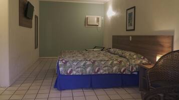 Un dormitorio con cama, una silla, aire acondicionado de pared y un cuadro en la pared.