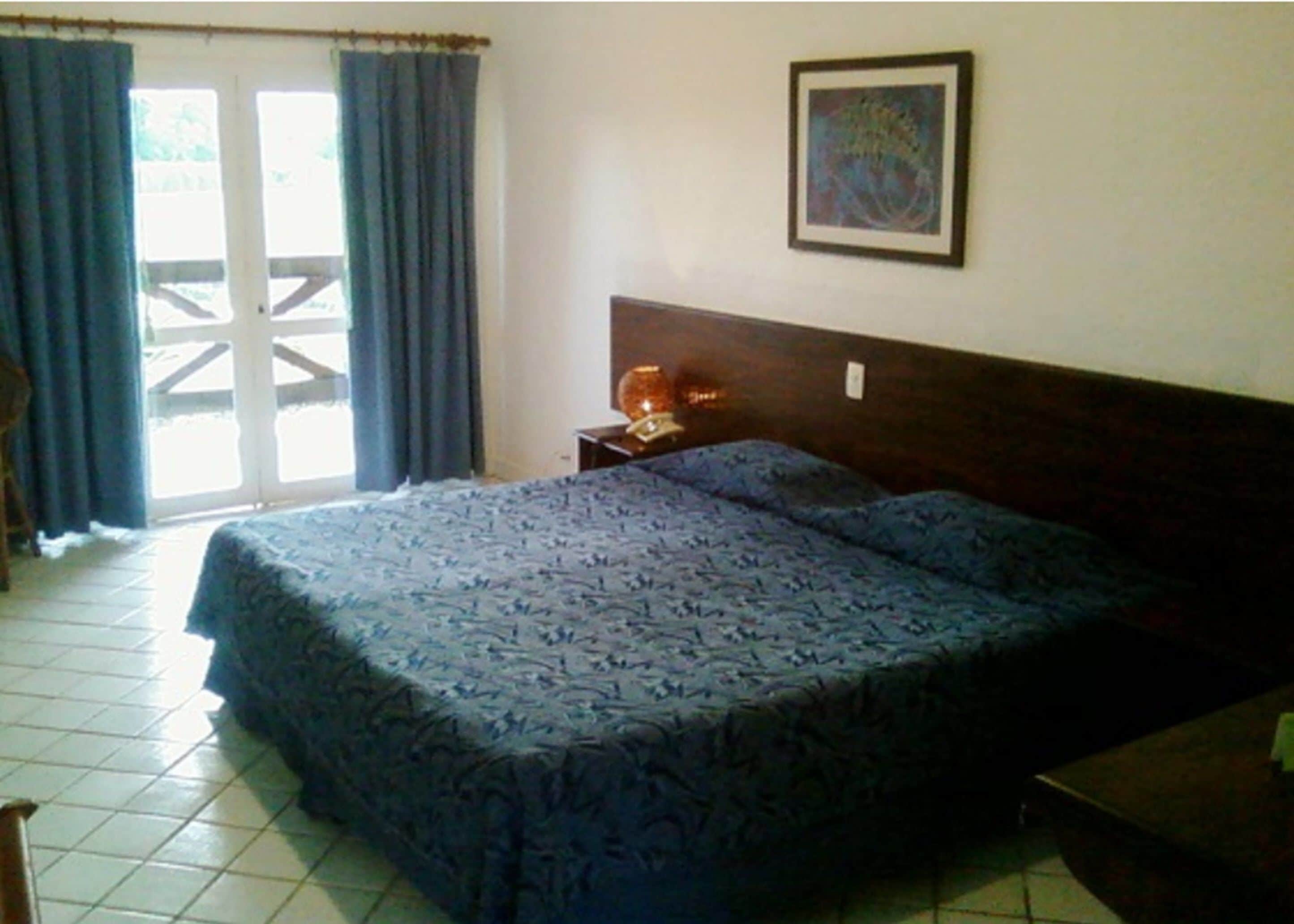 A bedroom with a bed, a nightstand, a framed picture on the wall, and a window with curtains.