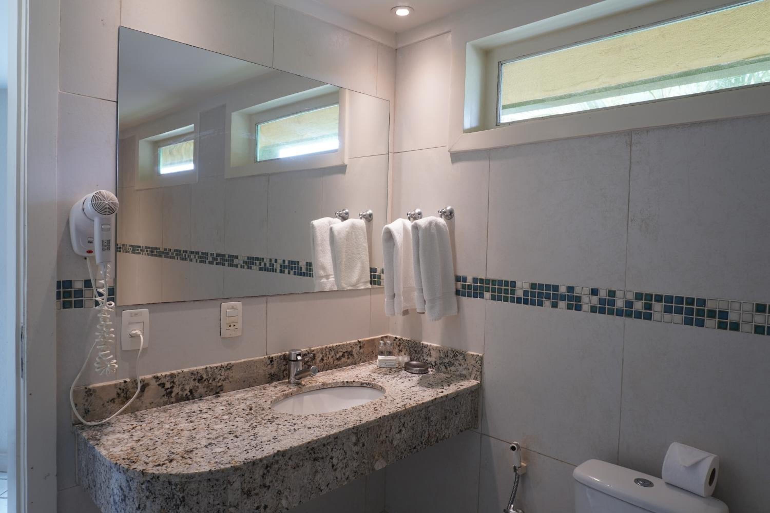 A bathroom with a granite sink, a mirror, a hairdryer, and a toilet.