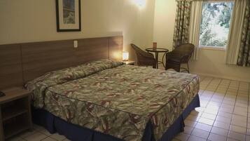 A bedroom with a bed, a nightstand, a chair, a small table, and a window with curtains.