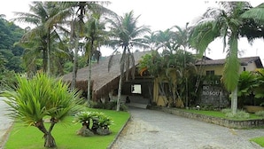 Un resort tropical con un edificio de techo de paja, palmeras y un muro de piedra.