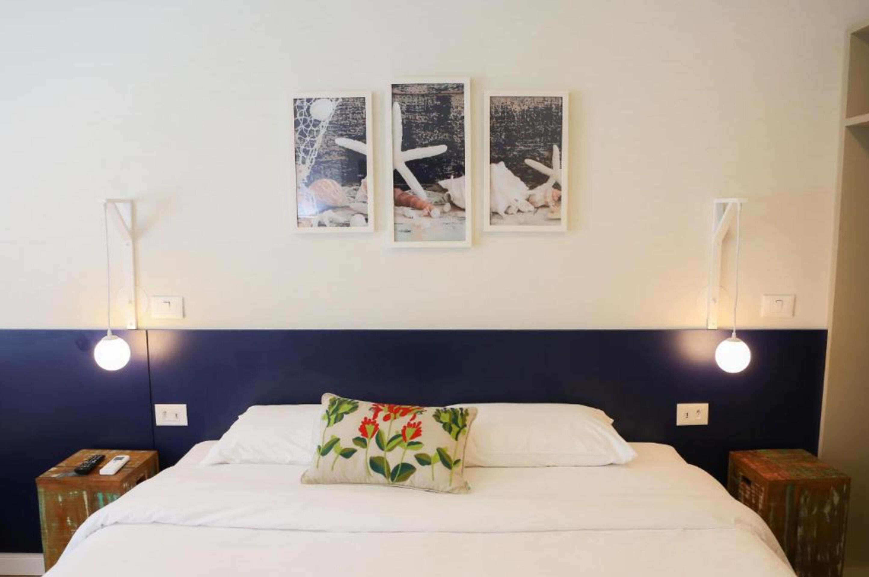 Ein Hotelzimmer mit einem Bett, einem Nachttisch, einer Lampe und drei gerahmten Bildern an der Wand.