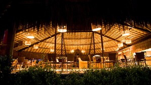 Un espacio de comedor al aire libre con techo de paja y varias mesas y sillas.