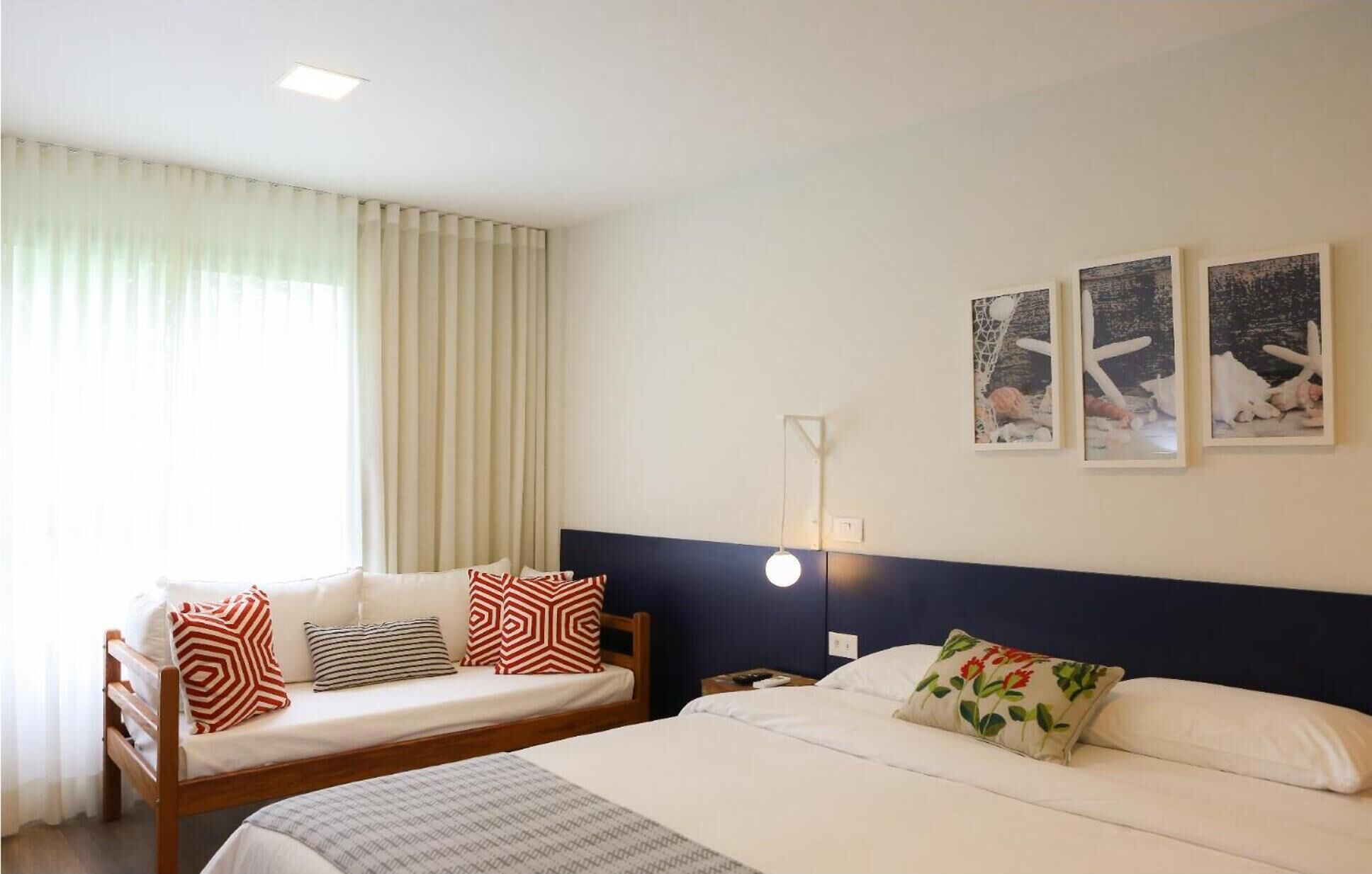 Une chambre d’hôtel avec deux lits, une grande fenêtre avec des rideaux et trois tableaux accrochés au mur.