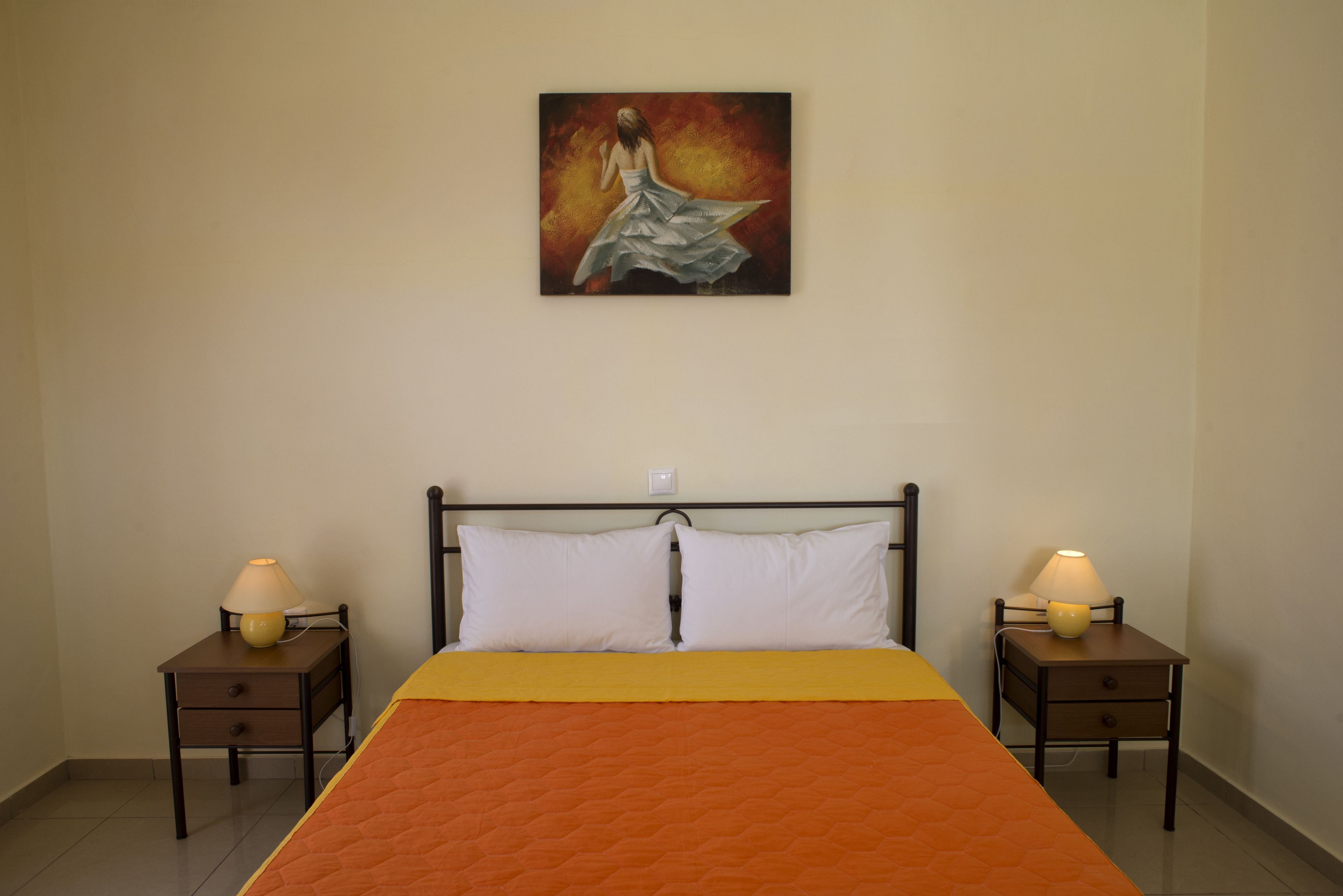 A bedroom with a bed, two bedside tables, two lamps, and a painting on the wall.