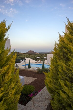 A pool area with lounge chairs and umbrellas, surrounded by greenery and white walls.