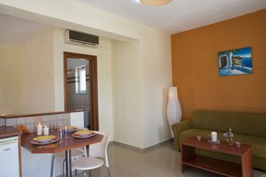 Un espace de vie compact comprenant un coin repas, un canapé vert et un tableau accroché au mur.